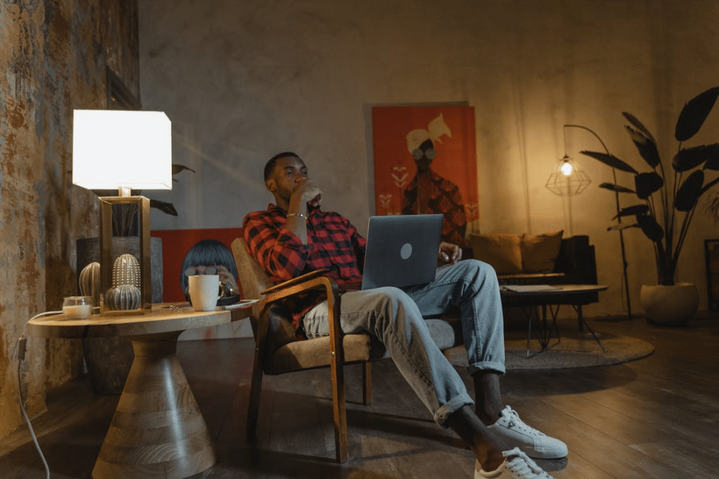 Man in Red and White Stripe Polo Shirt Sitting on Brown Wooden Chair Using Silver Laptop