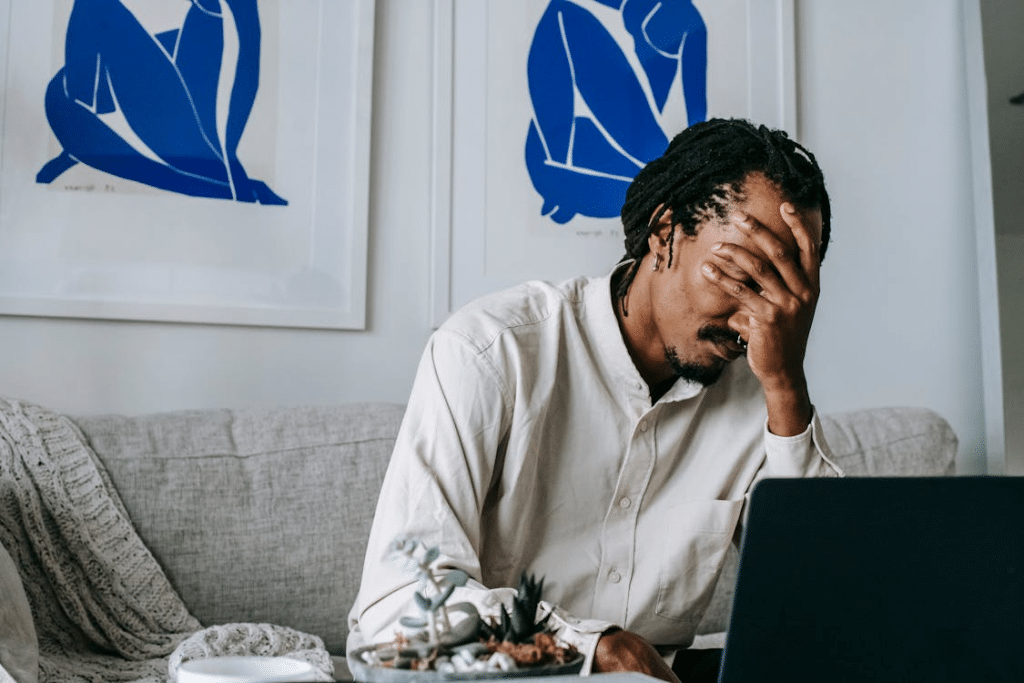 Upset young black guy covering face with hand while working remotely on netbook