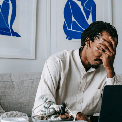 Upset young black guy covering face with hand while working remotely on netbook