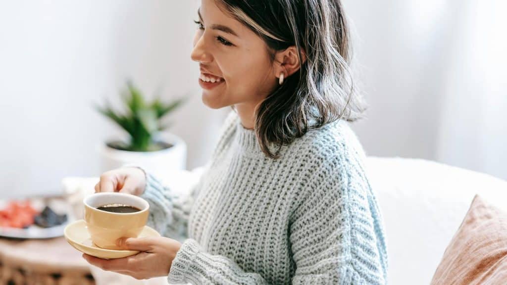 A smiling woman holding a cup of coffee while sitting indoors.