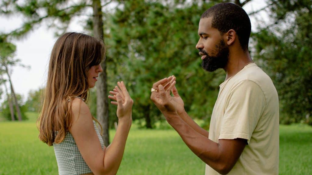 An animated couple making hand gestures while arguing outdoors.