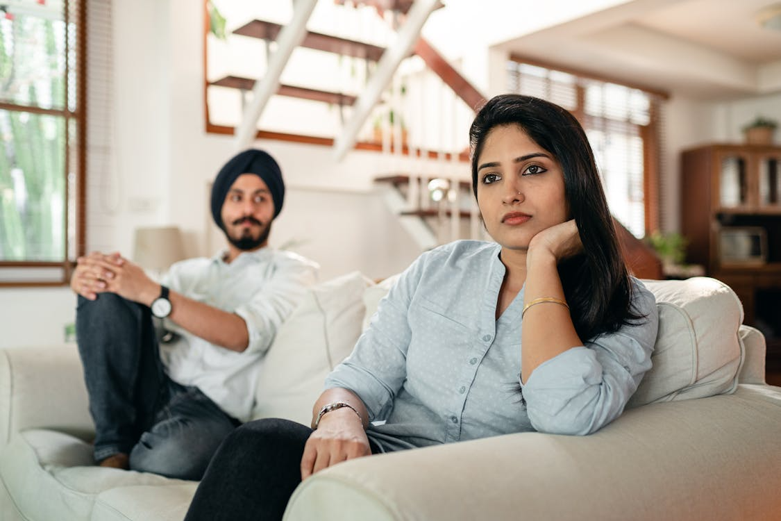 Offended young indian female sitting on couch with husband