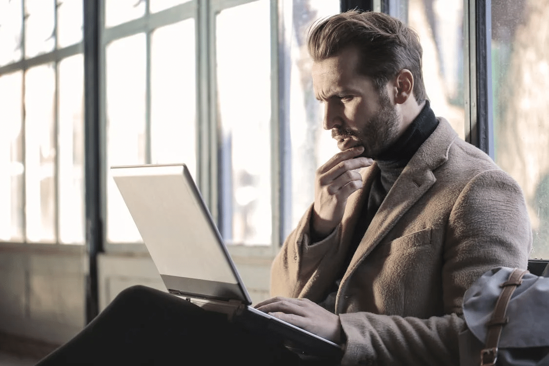 Man wearing brown jacket and using grey laptop