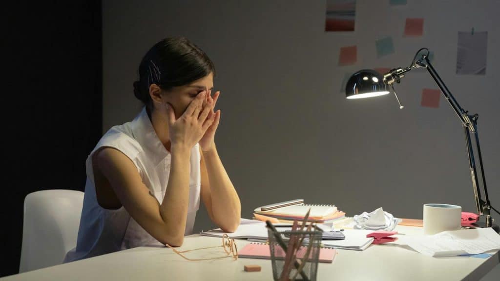 A person sitting at a desk with their face in their hands, appearing stressed or tired.