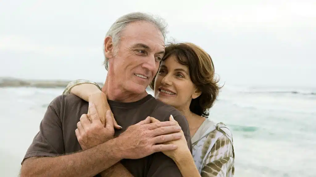 An older couple holding each other on the beach.