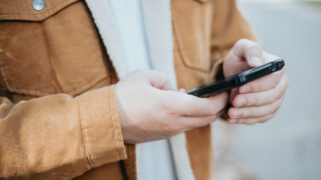 A closeup of a man in a tan jacket texting on his smartphone.
