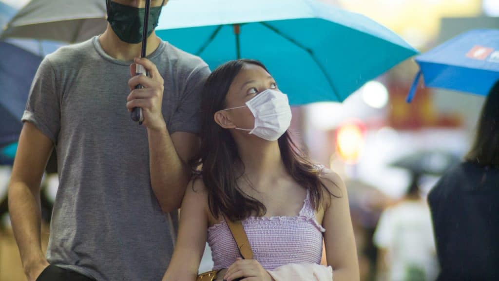 A man holding umbrella and a woman wearing mask is walking with him