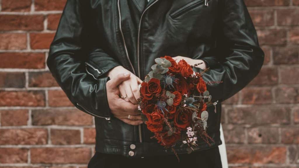 A couple wearing black jackets holding a bouquet of red roses.