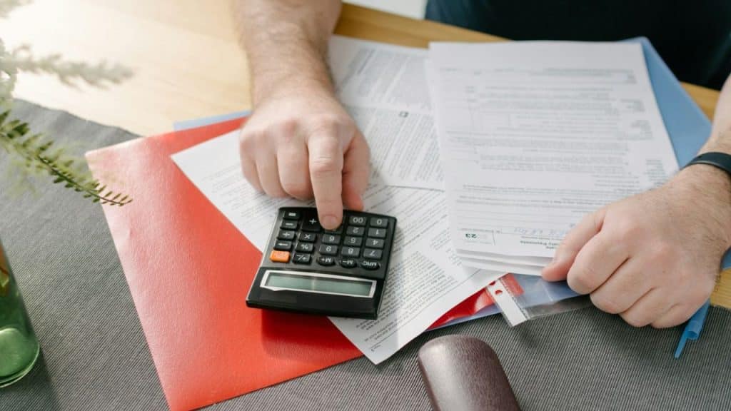 Close-up of hands using a calculator surrounded by documents on a table.