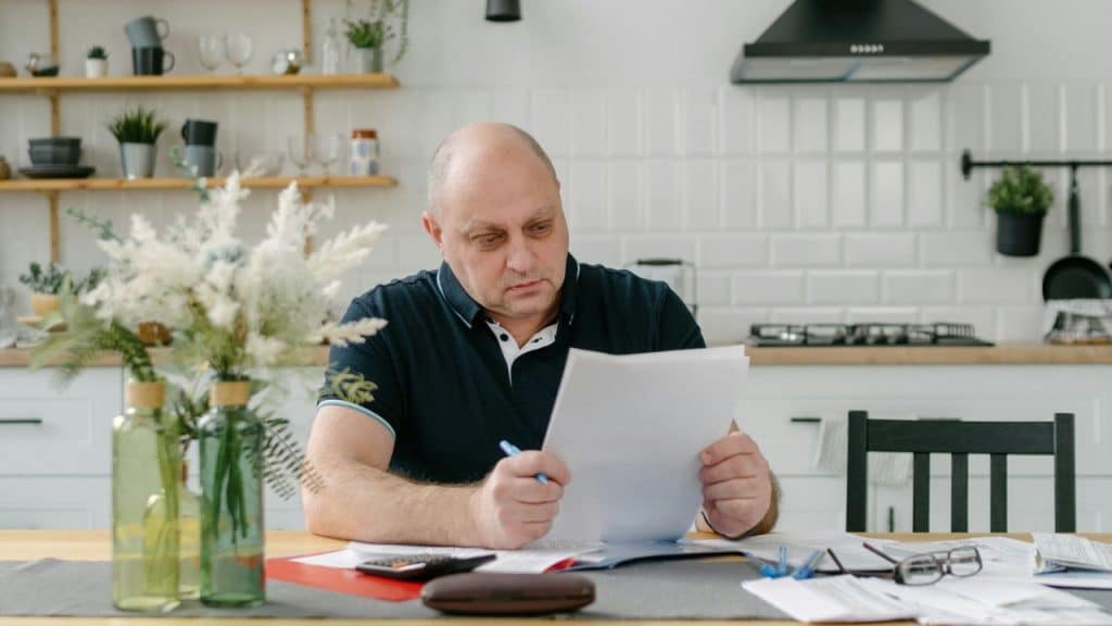 A man sitting at a kitchen table seriously examining a document with a pen.