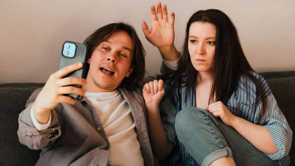 Two people making a video call; one waves while the other holds a phone.