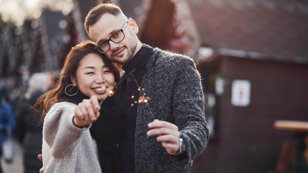 Young couple outdoors holding lit sparklers and smiling at the camera.
