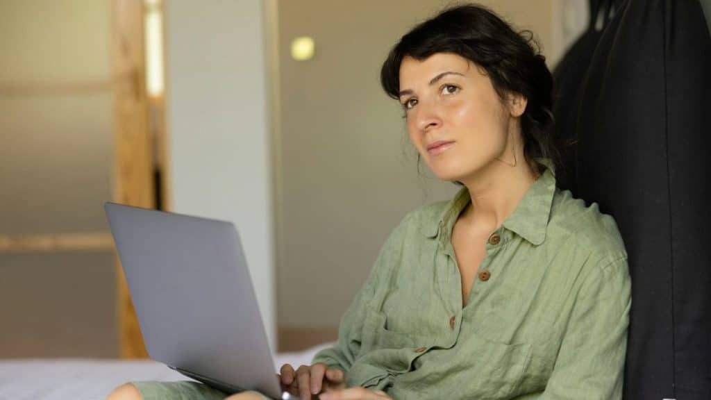 Woman in a green shirt sitting with a laptop, looking off into the distance.