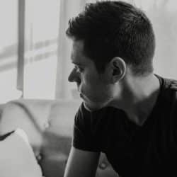 Black and white close-up of a man sitting on a sofa looking out a window.