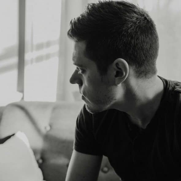 Black and white close-up of a man sitting on a sofa looking out a window.