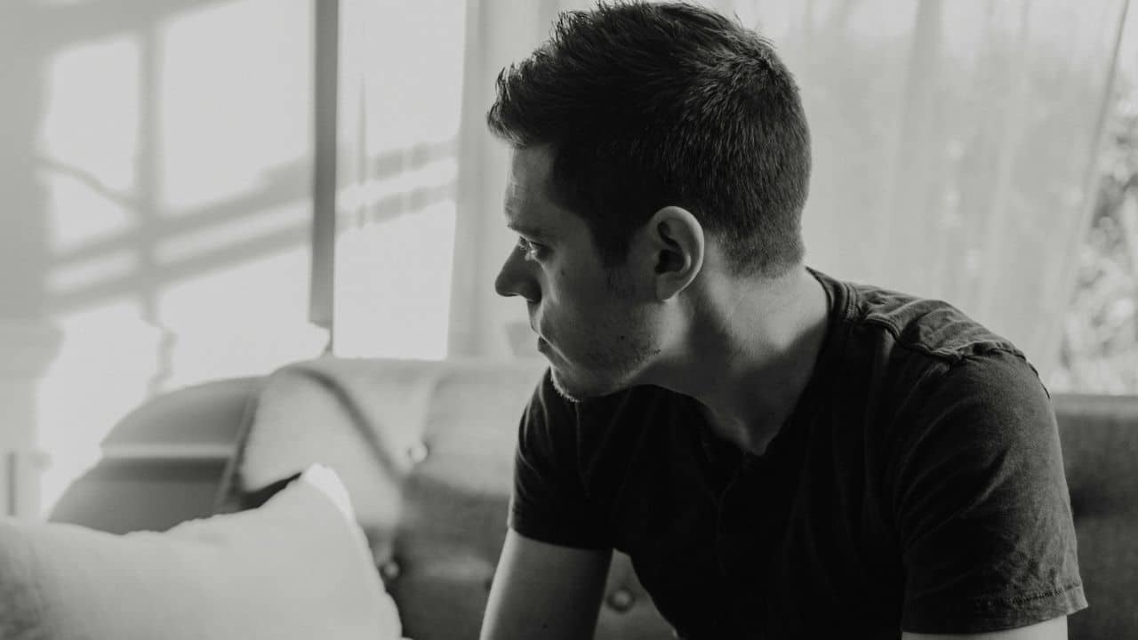 Black and white close-up of a man sitting on a sofa looking out a window.