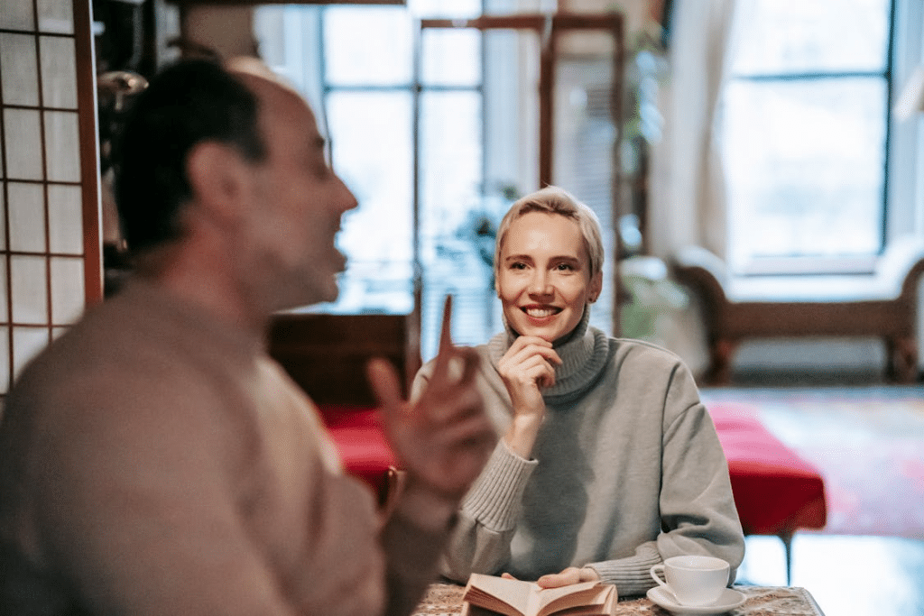 Anonymous man talking to cheerful wife smiling while reading book at table