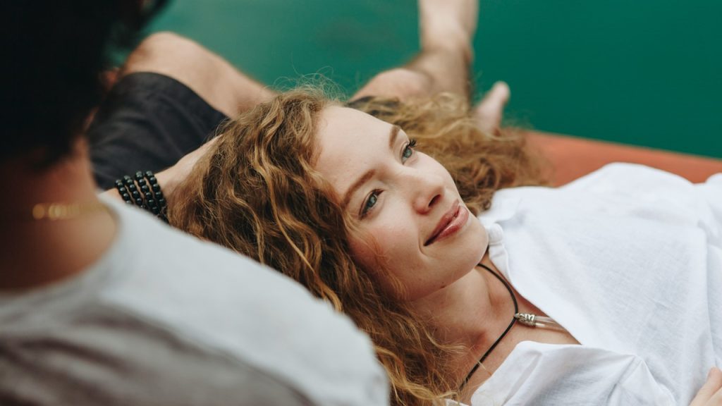 A woman with her head on a man's thighs and looking lost in thought.