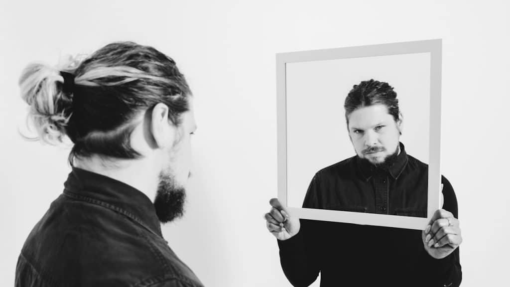 A man looking at his reflection in a mirror held by another person.