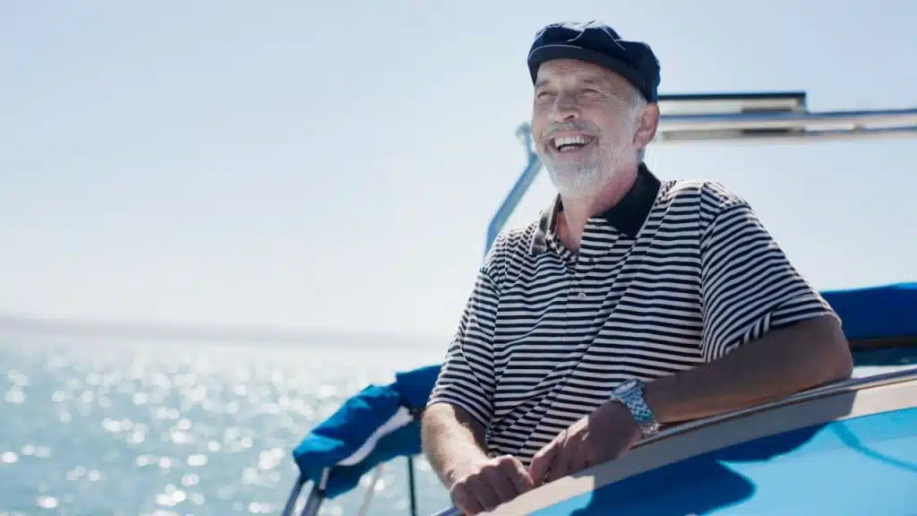 Smiling older man in a striped shirt and cap on a boat on the water.
