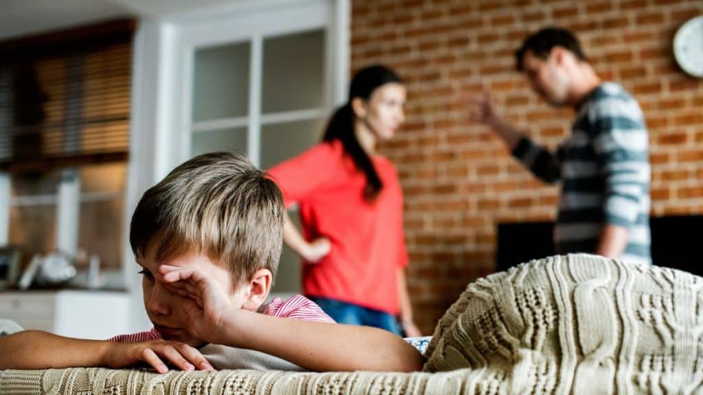 Distraught child in the foreground while two adults argue in the background.