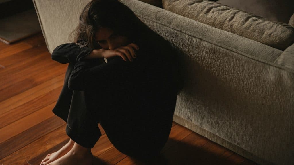A woman sitting on the floor and crying while leaning on a couch.