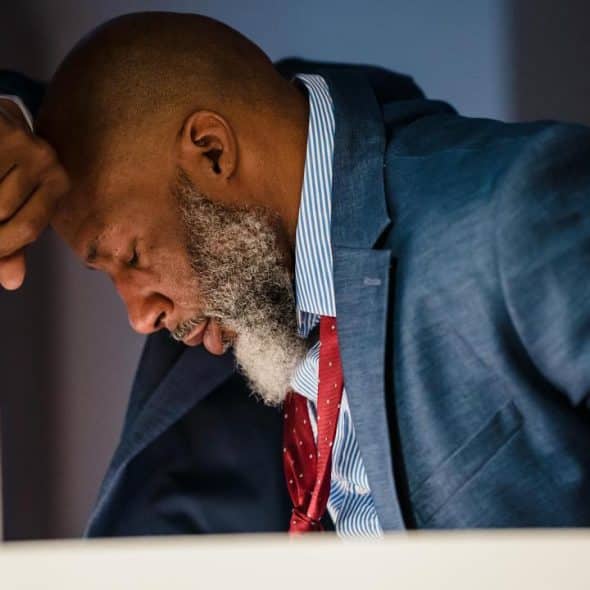 A man in a suit leaning forward with his head down, appearing stressed or exhausted.