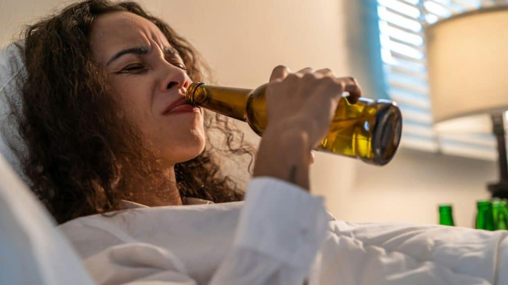 Woman with long curly hair taking a large drink directly from a brown beer bottle.