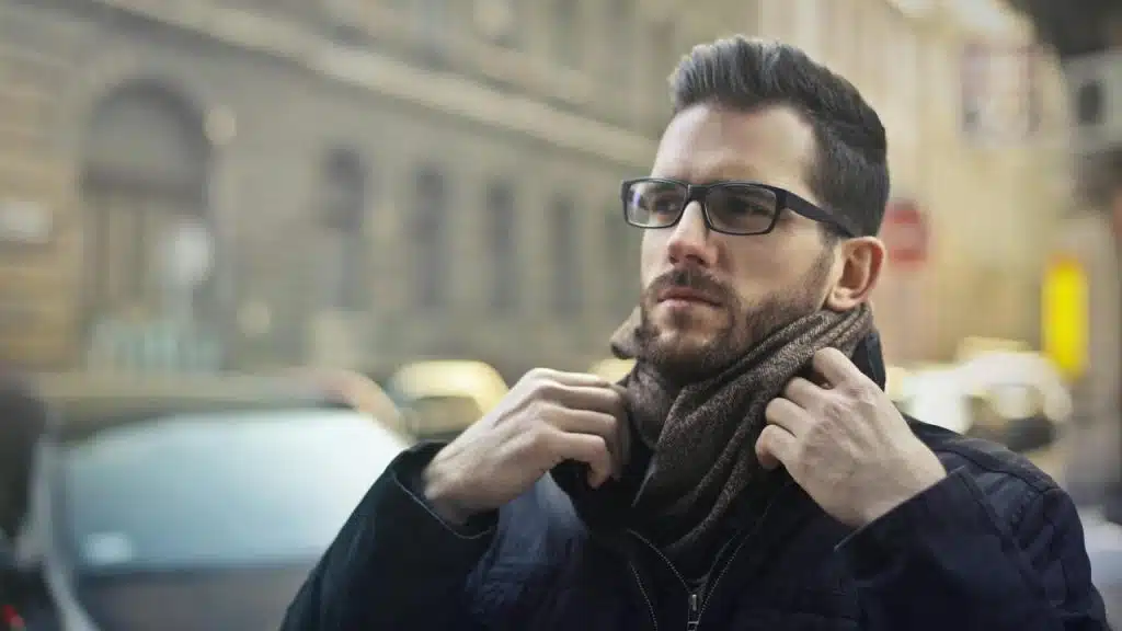 A man adjusting his scarf while standing outdoors in a city street.