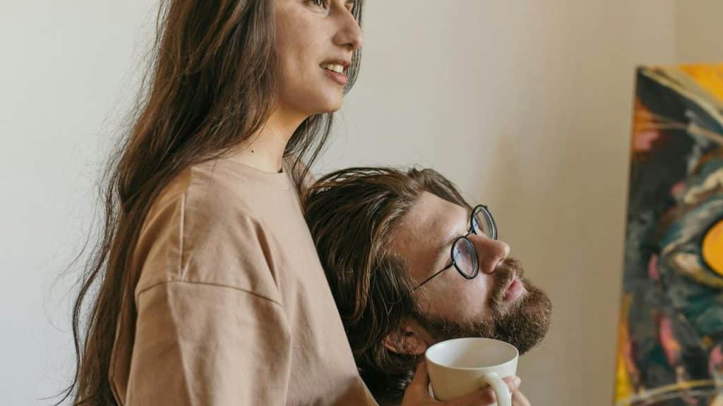 A couple relaxing together, one holding a cup and leaning affectionately on the other.
