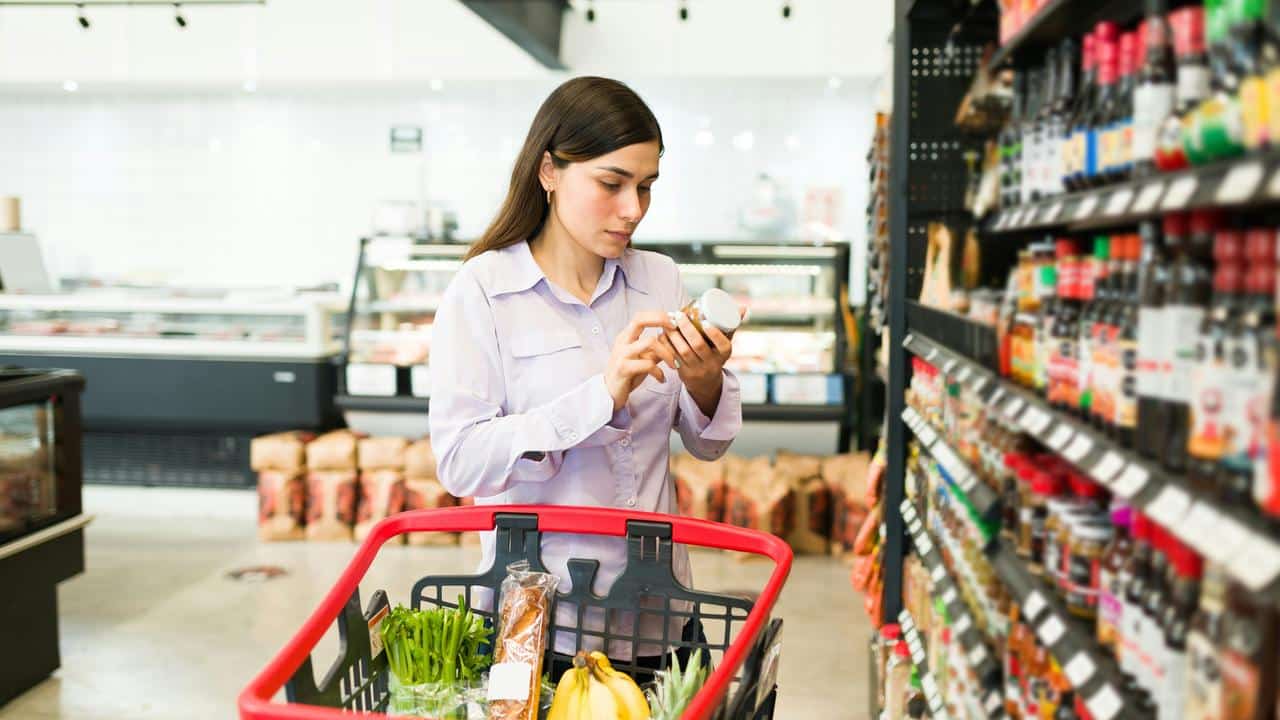 A woman reading a product label while shopping in a grocery store.