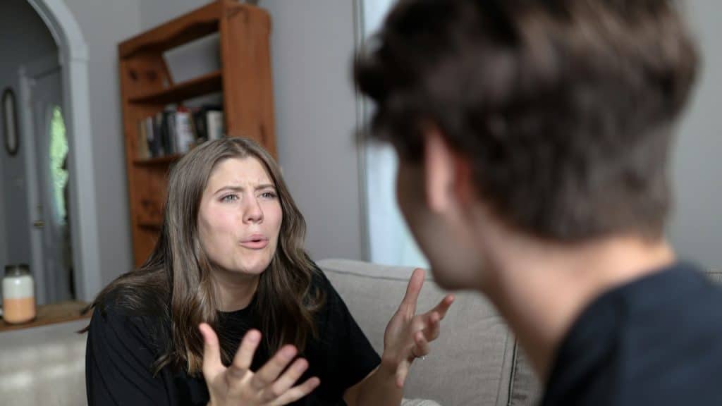 A woman complaining to her husband while sitting on a couch with her husband.