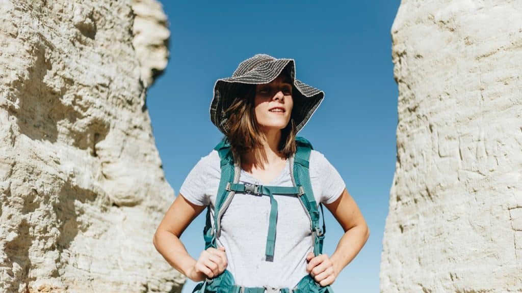 A woman standing in a hilly area with a backpack.