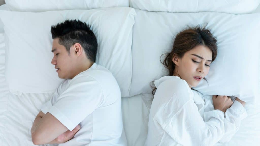Young couple lying down on bed with painful expressions.
