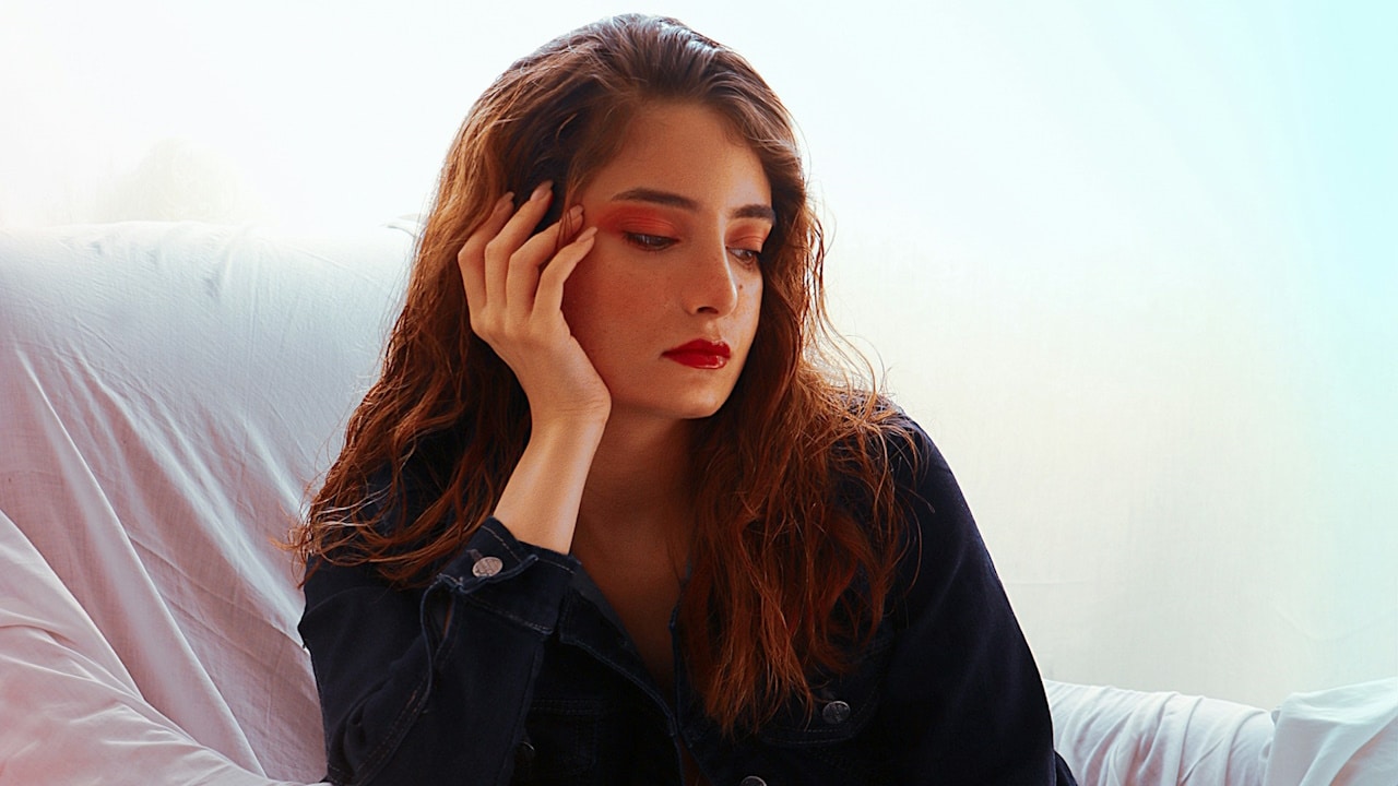 A woman sitting on a couch with her hand on her head.