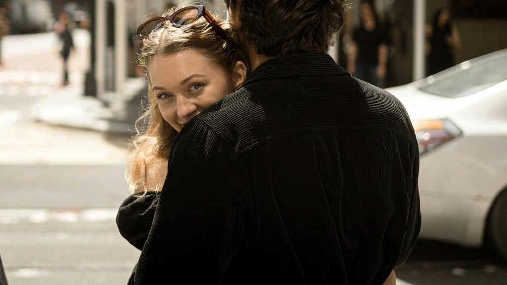 A woman smiling warmly while hugging someone on a city street.