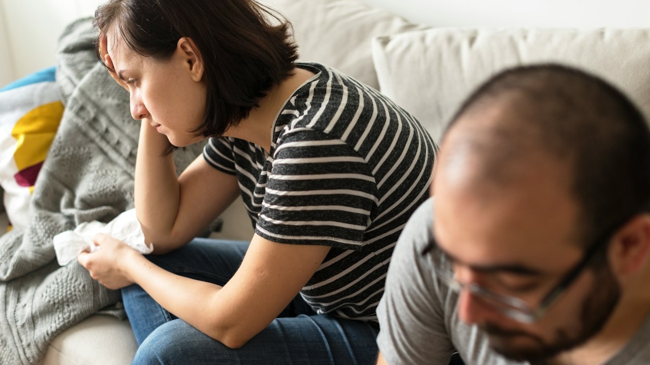 An unhappy couple sitting on a couch after having an argument.
