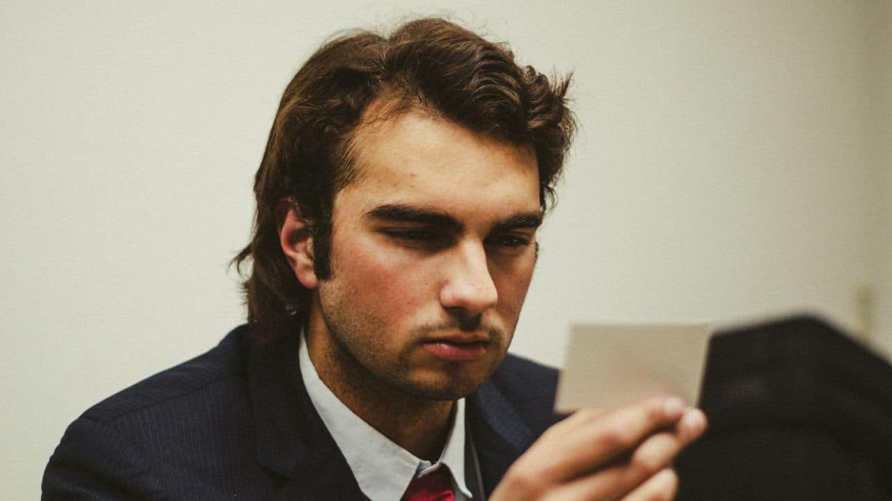 A young man in a suit and tie looks closely at a small white card.