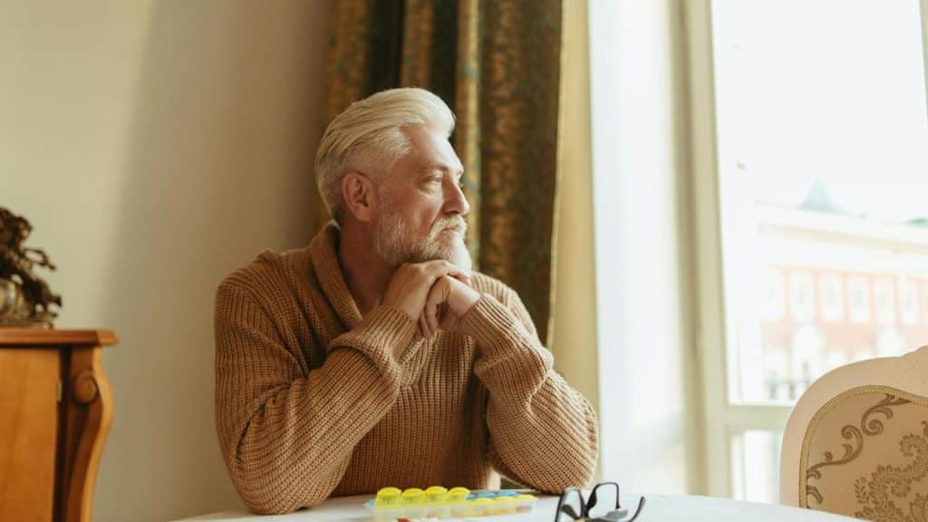 An older man sitting at a table and looking thoughtfully out the window.
