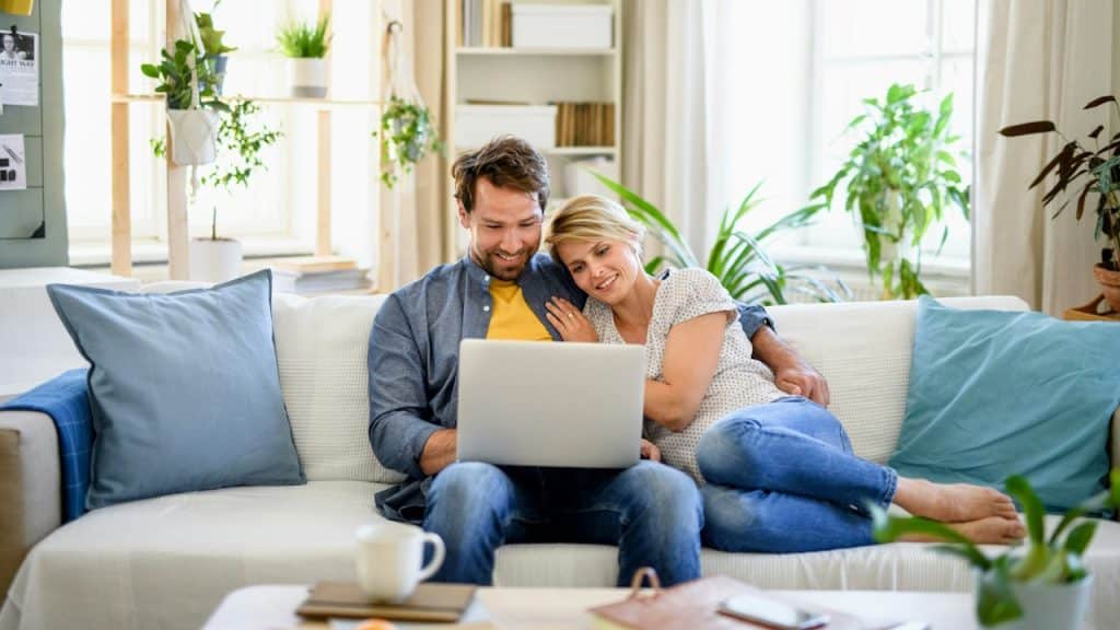 A couple sitting on a couch and looking at a laptop.