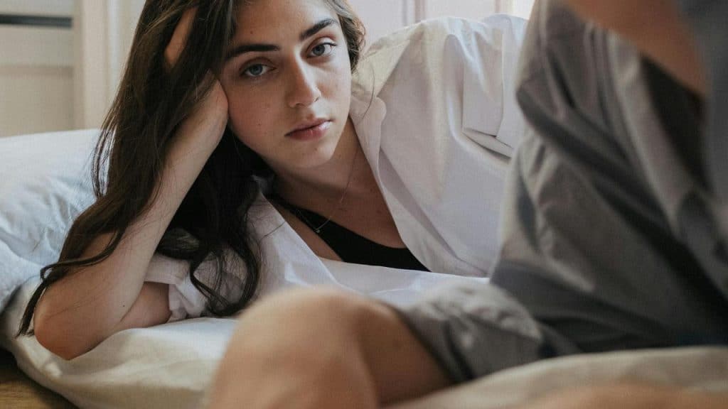 A woman lying on a bed with her head resting on her hand, looking thoughtful.