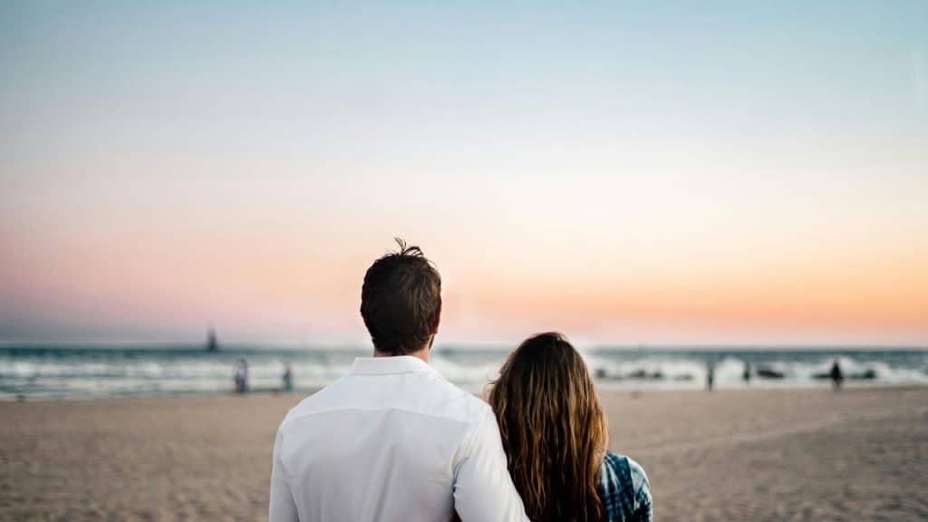 A couple standing on the beach watching the sunset.