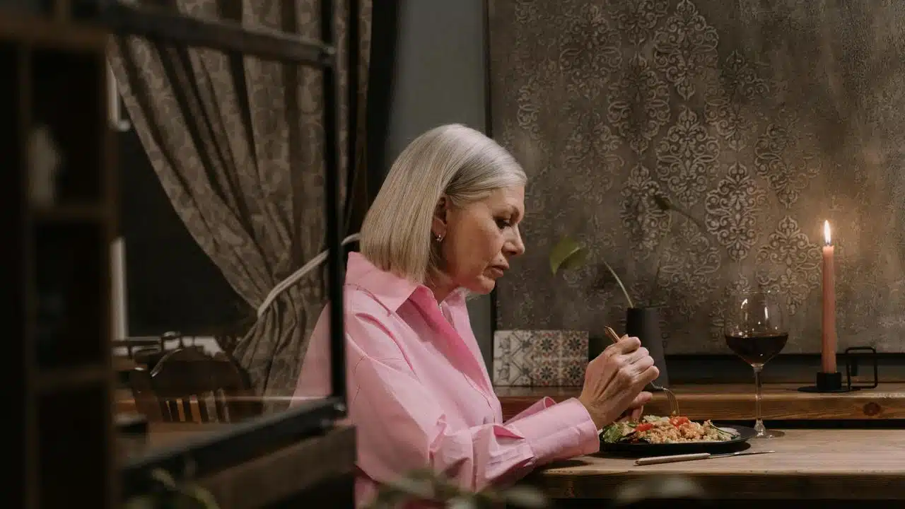 An older woman eating a meal at a dimly lit table.