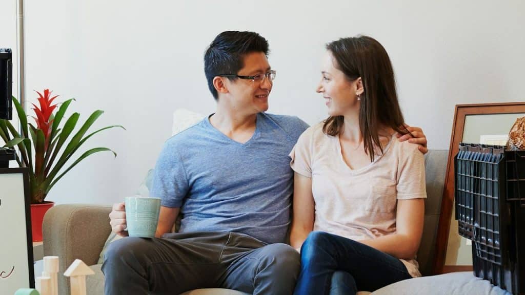Couple sitting close on a couch, looking and smiling at each other.