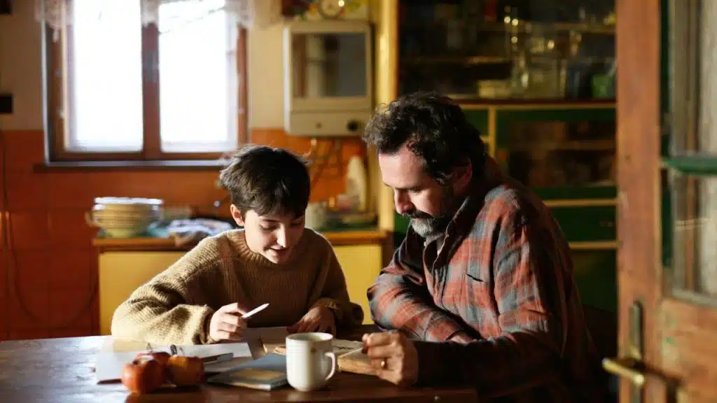 A man and a young boy sit at a wooden table reading and studying together.