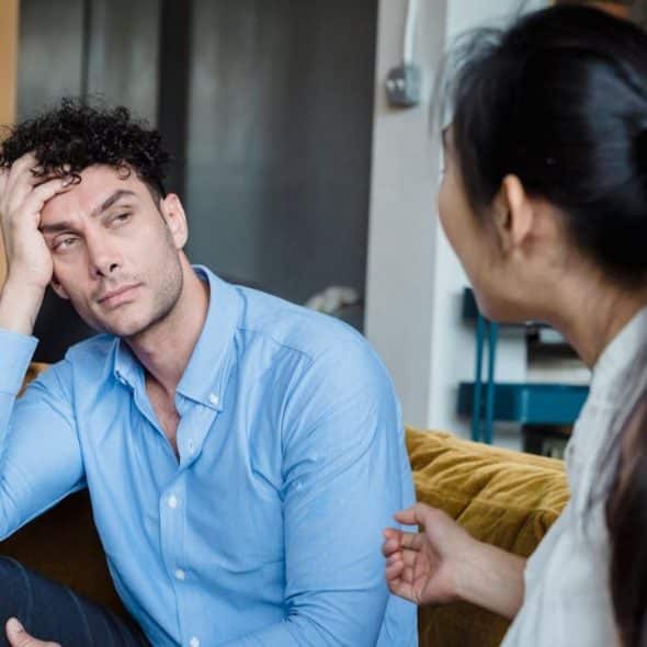 A man looks frustrated, resting his head on his hand while a woman talks to him.