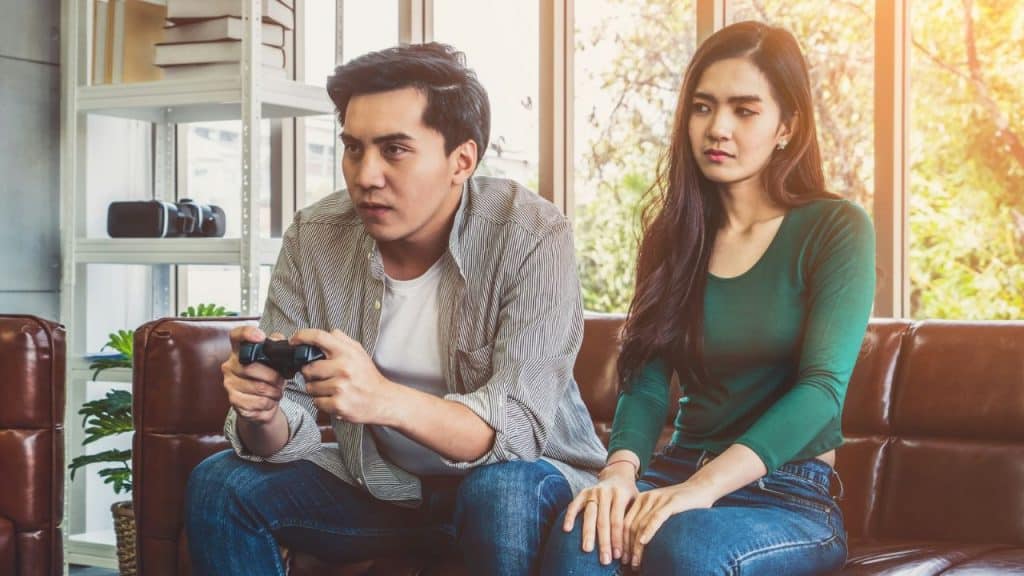 Man playing a video game on a couch next to a woman looking serious.