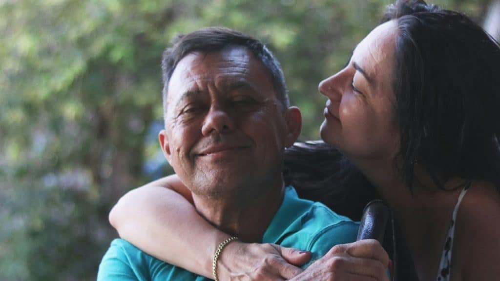 A woman in a black and yellow tank top is hugging a man in a green polo shirt.