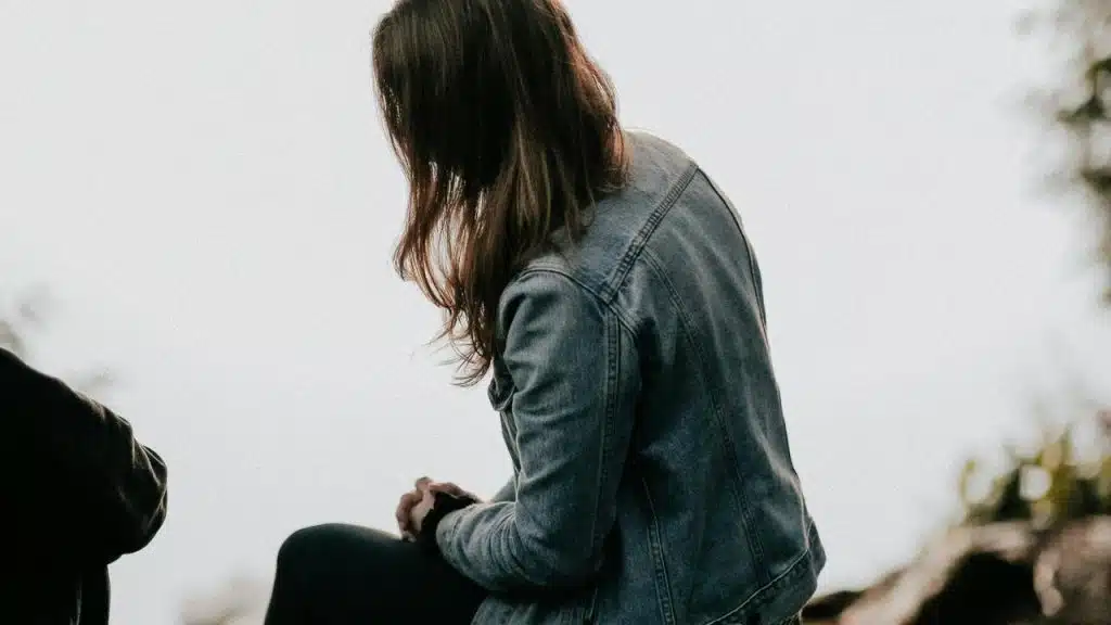 A woman wearing a denim jacket sitting outdoors and looking down.
