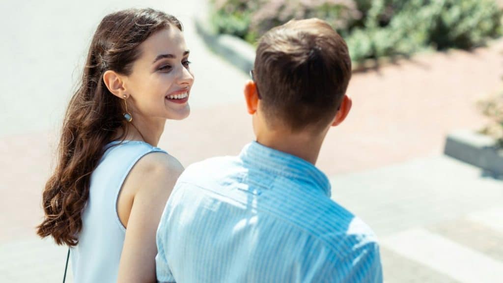 Smiling woman with long brown hair looking at a man from behind outdoors.